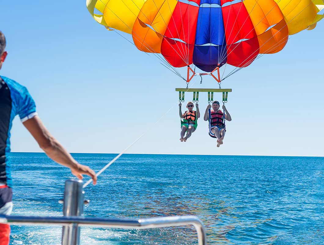 Two guests parasailing beneath a colorful canopy above Gulf water with Anna Maria Island Parasail.